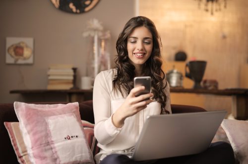 woman-sitting-on-sofa-while-looking-at-phone-with-laptop-on-920382